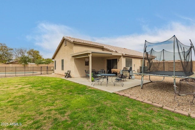 back of property with a fenced backyard, a trampoline, a yard, a patio area, and stucco siding