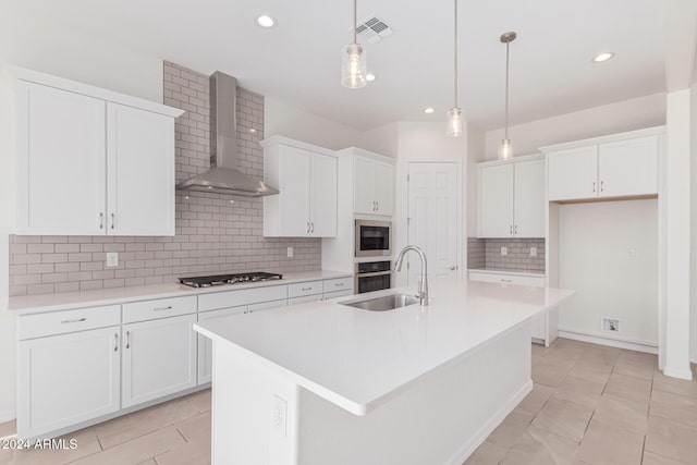 kitchen featuring wall chimney exhaust hood, stainless steel appliances, sink, a center island with sink, and white cabinets