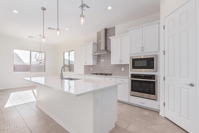 kitchen featuring a center island with sink, wall chimney range hood, sink, and appliances with stainless steel finishes