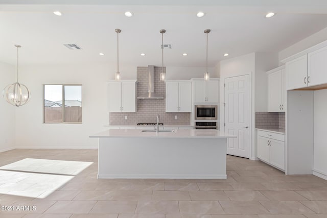 kitchen featuring stainless steel appliances, a kitchen island with sink, hanging light fixtures, and wall chimney range hood