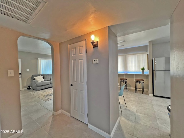 hallway with tile patterned floors, visible vents, arched walkways, and baseboards