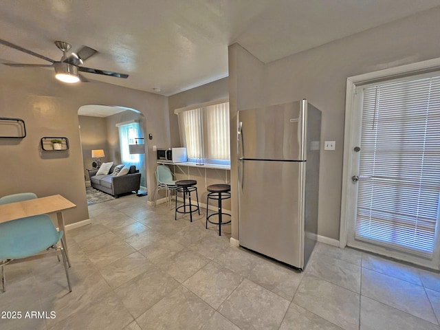 kitchen with baseboards, arched walkways, freestanding refrigerator, ceiling fan, and a kitchen breakfast bar