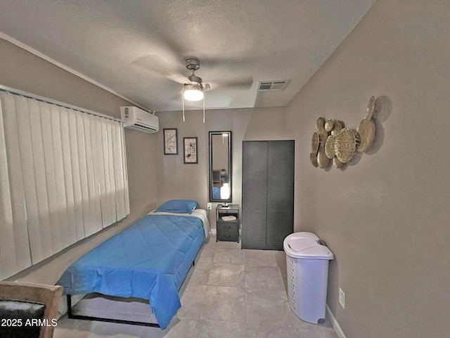 bedroom with a wall mounted air conditioner, visible vents, a textured ceiling, baseboards, and ceiling fan