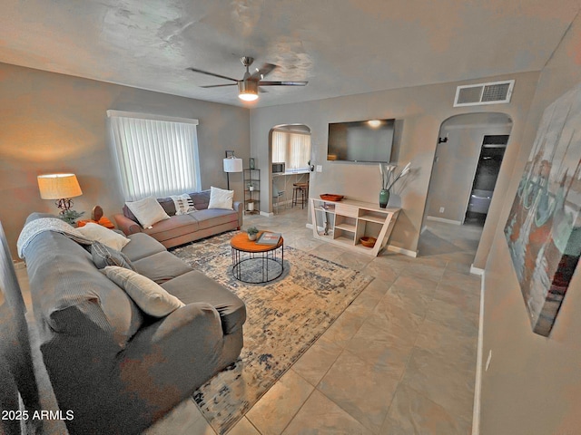 living area featuring visible vents, arched walkways, baseboards, and ceiling fan