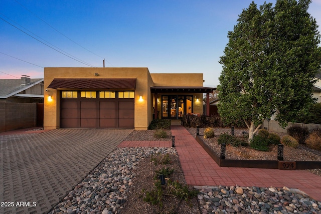 pueblo revival-style home with a garage, decorative driveway, fence, and stucco siding