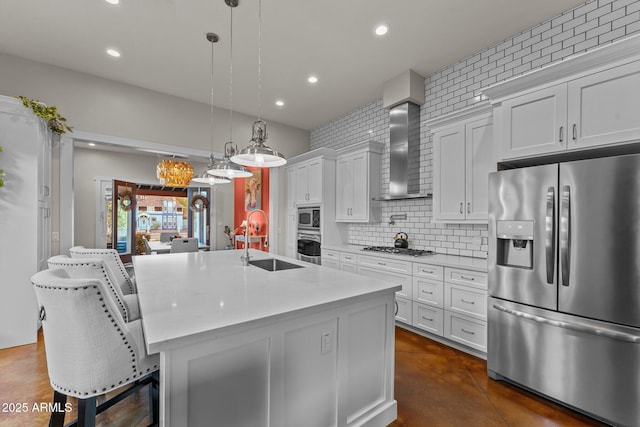 kitchen with an island with sink, wall chimney exhaust hood, backsplash, stainless steel appliances, and a sink