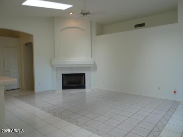 unfurnished living room with light tile patterned floors, baseboards, a large fireplace, and ceiling fan