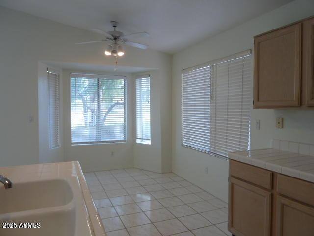 interior space with a sink, tile counters, a ceiling fan, and light tile patterned floors