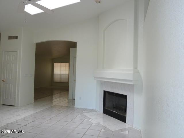 unfurnished living room with visible vents, a ceiling fan, a glass covered fireplace, arched walkways, and light tile patterned floors