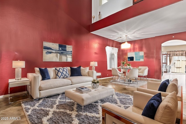 living area with baseboards, arched walkways, and a high ceiling