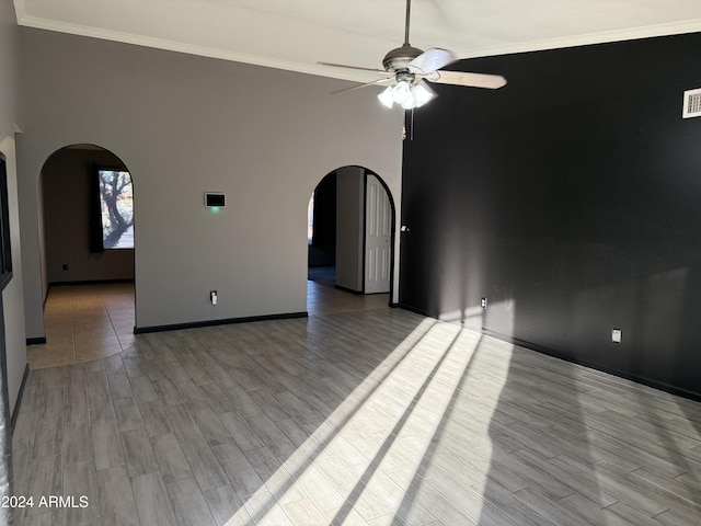 empty room with hardwood / wood-style flooring, ceiling fan, ornamental molding, and a high ceiling