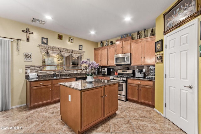 kitchen with sink, backsplash, dark stone countertops, a kitchen island, and appliances with stainless steel finishes