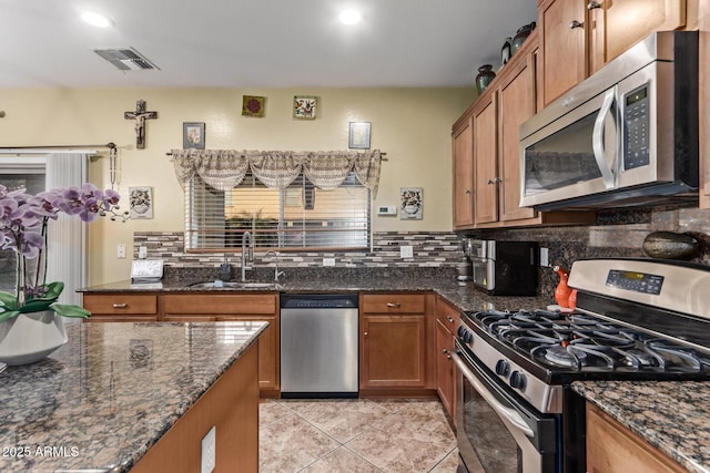 kitchen featuring appliances with stainless steel finishes, tasteful backsplash, dark stone counters, sink, and light tile patterned flooring