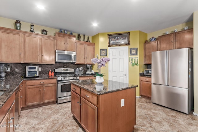 kitchen featuring decorative backsplash, stainless steel appliances, a kitchen island, and dark stone countertops