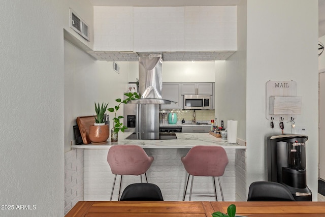 kitchen featuring a kitchen bar, island exhaust hood, kitchen peninsula, backsplash, and black electric stovetop