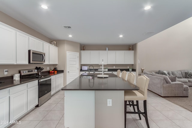 kitchen featuring white cabinets, an island with sink, sink, appliances with stainless steel finishes, and a breakfast bar area