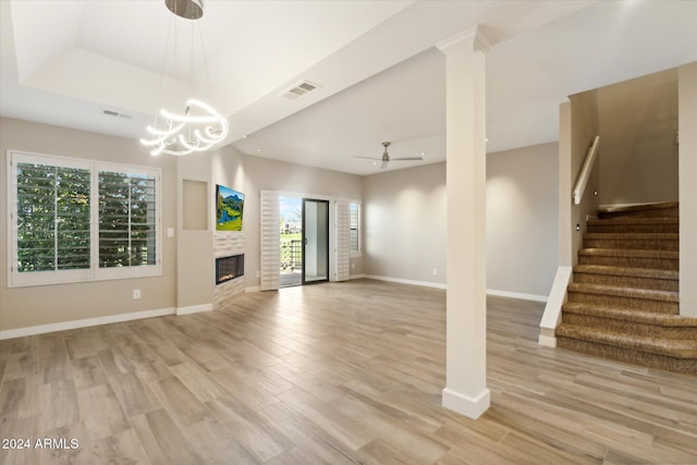 unfurnished living room with a fireplace, ceiling fan with notable chandelier, light hardwood / wood-style floors, and a healthy amount of sunlight