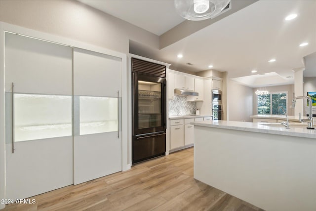 kitchen featuring white cabinets, built in appliances, light wood-type flooring, and tasteful backsplash