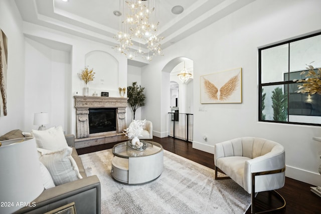 living room with a fireplace, a tray ceiling, a chandelier, and dark wood-type flooring