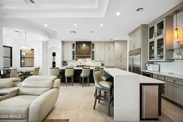 kitchen featuring custom exhaust hood, a center island with sink, built in refrigerator, decorative backsplash, and decorative light fixtures