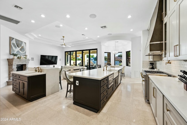 kitchen featuring custom range hood, ceiling fan with notable chandelier, stainless steel appliances, a kitchen island with sink, and white cabinets