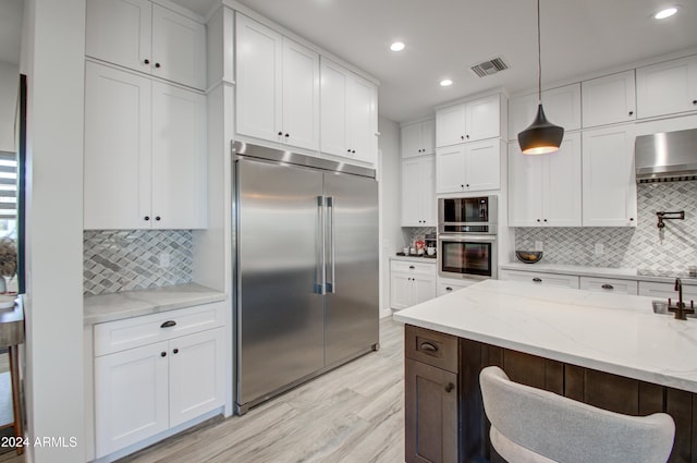 kitchen featuring built in appliances, white cabinetry, light stone counters, and decorative light fixtures