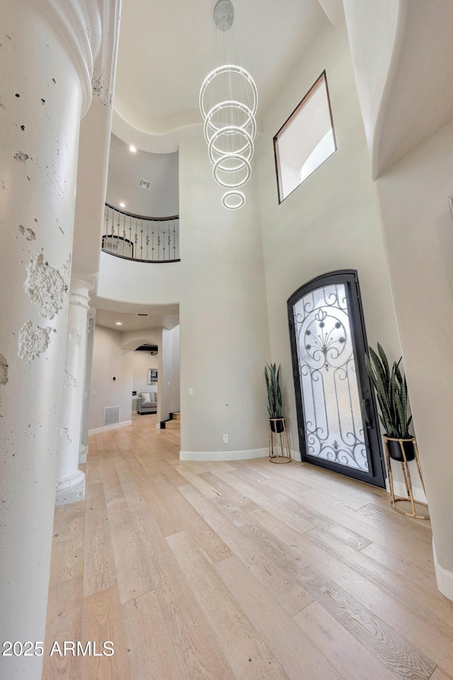 entrance foyer featuring a towering ceiling, visible vents, a chandelier, and wood finished floors