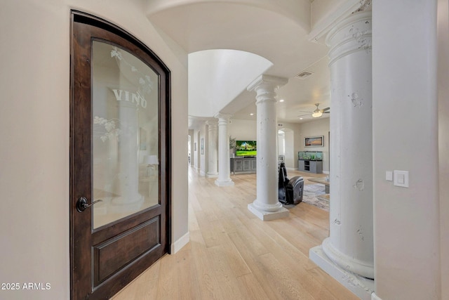 foyer entrance featuring arched walkways, a ceiling fan, visible vents, light wood finished floors, and ornate columns