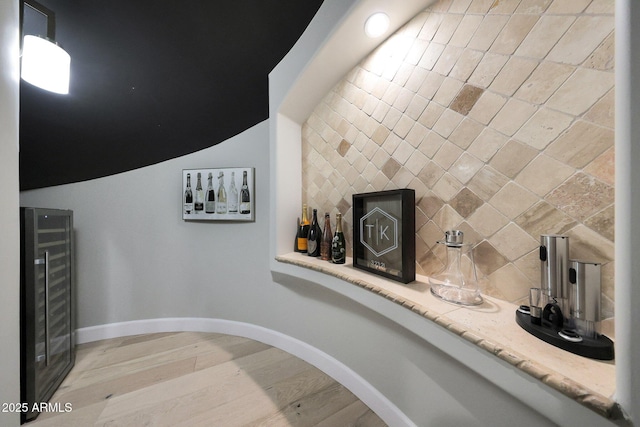 details featuring wine cooler, a dry bar, backsplash, wood finished floors, and baseboards