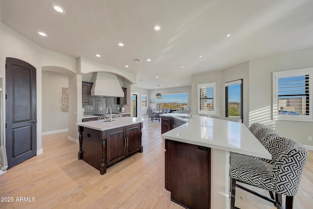 kitchen with a spacious island, light countertops, dark brown cabinetry, and premium range hood