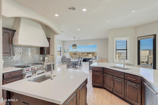 kitchen with a center island with sink, custom exhaust hood, visible vents, a sink, and double oven range