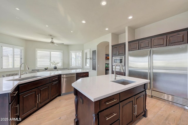 kitchen featuring built in appliances, light countertops, an island with sink, and a sink