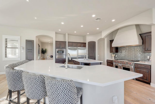 kitchen with light countertops, custom exhaust hood, and a large island with sink