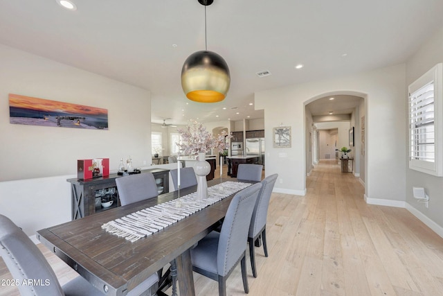 dining room with arched walkways, light wood finished floors, recessed lighting, visible vents, and baseboards