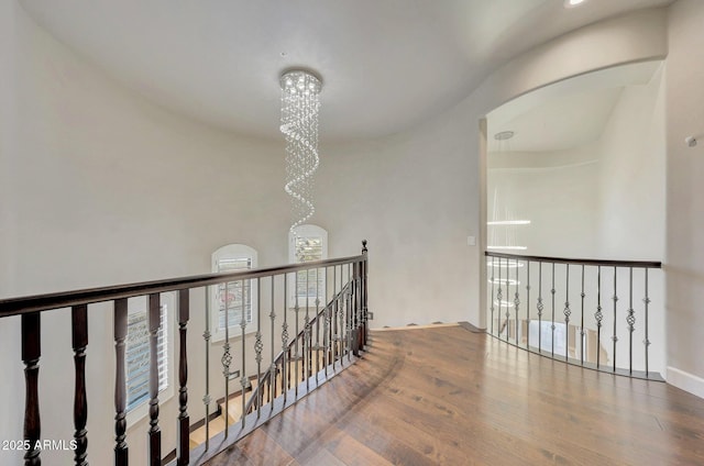 hallway with baseboards, arched walkways, wood finished floors, an upstairs landing, and a chandelier