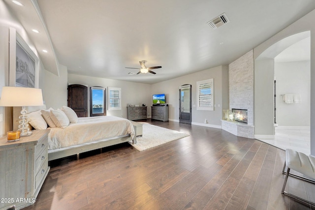 bedroom featuring arched walkways, a fireplace, visible vents, dark wood-type flooring, and baseboards