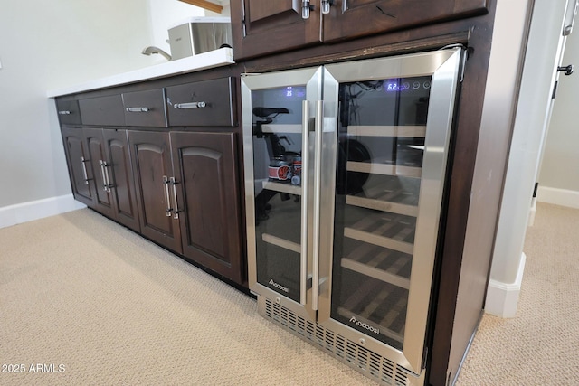 interior details with light colored carpet, beverage cooler, baseboards, and dark brown cabinets