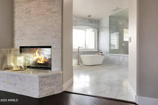 full bath with a soaking tub, visible vents, a stone fireplace, and baseboards