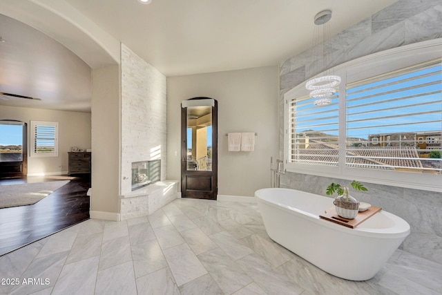 full bathroom with a freestanding tub, baseboards, marble finish floor, and a stone fireplace