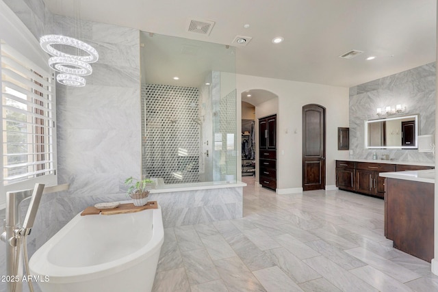 bathroom with a spacious closet, vanity, visible vents, and tile walls