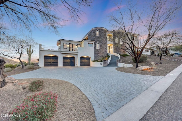 view of front of house with an attached garage, a balcony, stone siding, decorative driveway, and stucco siding