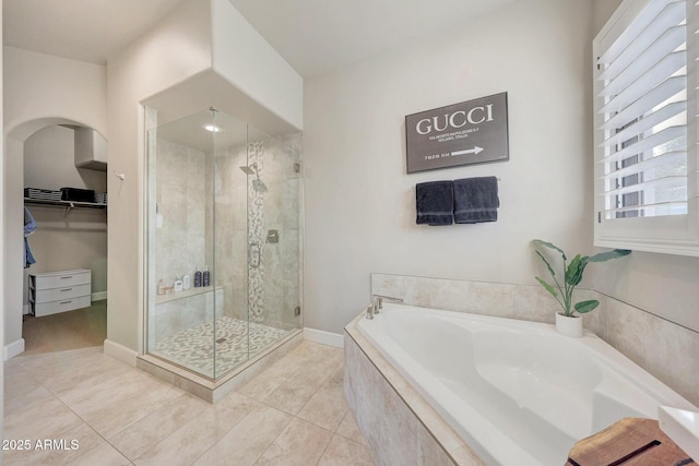 full bath featuring tile patterned flooring, a garden tub, baseboards, a spacious closet, and a stall shower