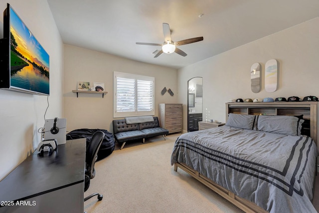 bedroom featuring ceiling fan, arched walkways, connected bathroom, and light colored carpet