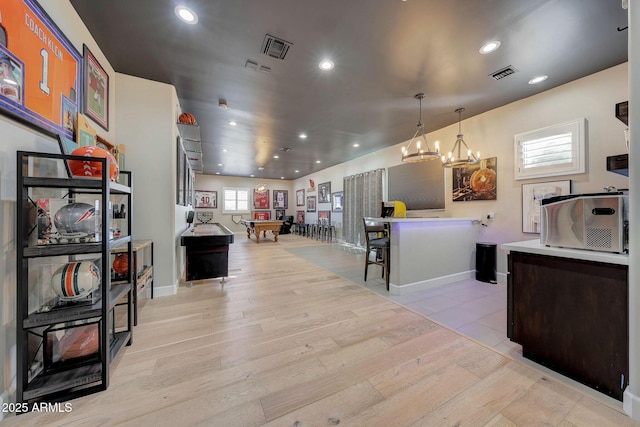 kitchen with light wood-style floors, visible vents, a kitchen breakfast bar, and decorative light fixtures