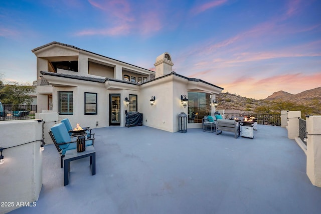 back of property at dusk with an outdoor living space with a fire pit, a patio area, a mountain view, and fence