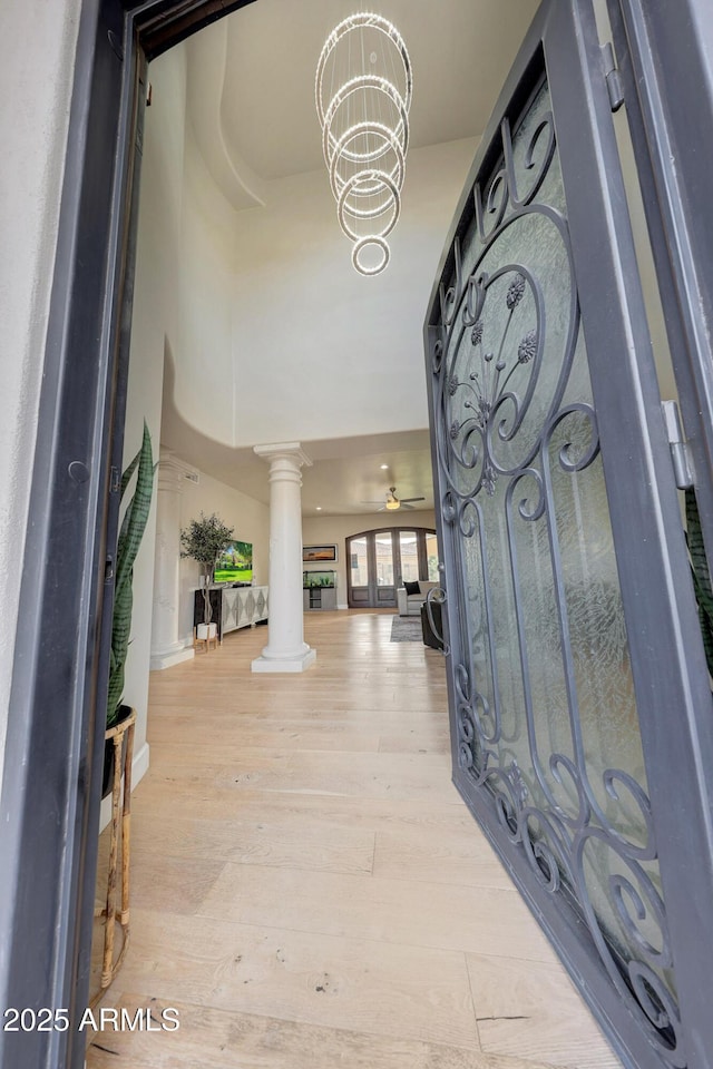 entryway featuring light wood-type flooring, ornate columns, a towering ceiling, and an inviting chandelier