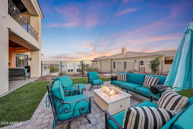 patio terrace at dusk featuring an outdoor living space with a fire pit, fence, and a balcony