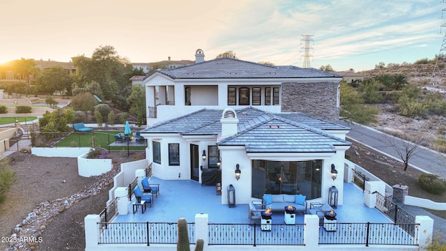 back of property at dusk featuring a tile roof, outdoor lounge area, a fenced backyard, and stucco siding