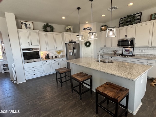 kitchen featuring sink, white cabinetry, decorative light fixtures, appliances with stainless steel finishes, and an island with sink