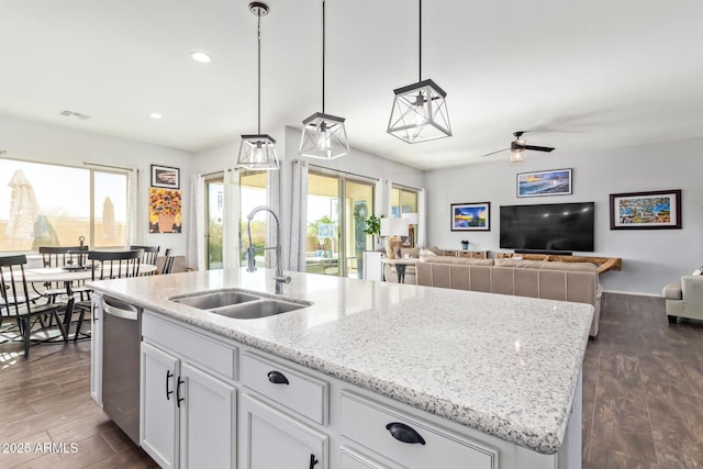 kitchen featuring dark wood-type flooring, sink, white cabinetry, decorative light fixtures, and a center island with sink